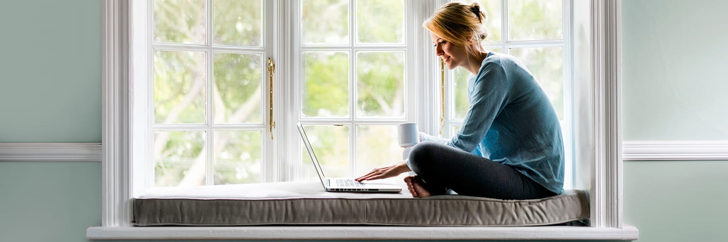 Woman in bay window looking at thegashub.co.nz on laptop
