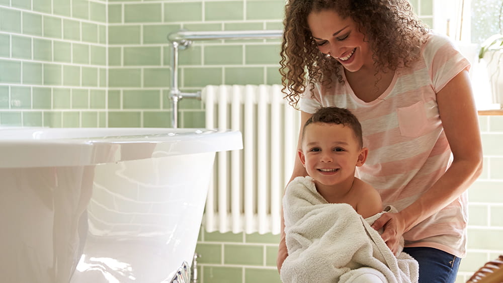 Mother and son in bathroom with radiator central heating warming them