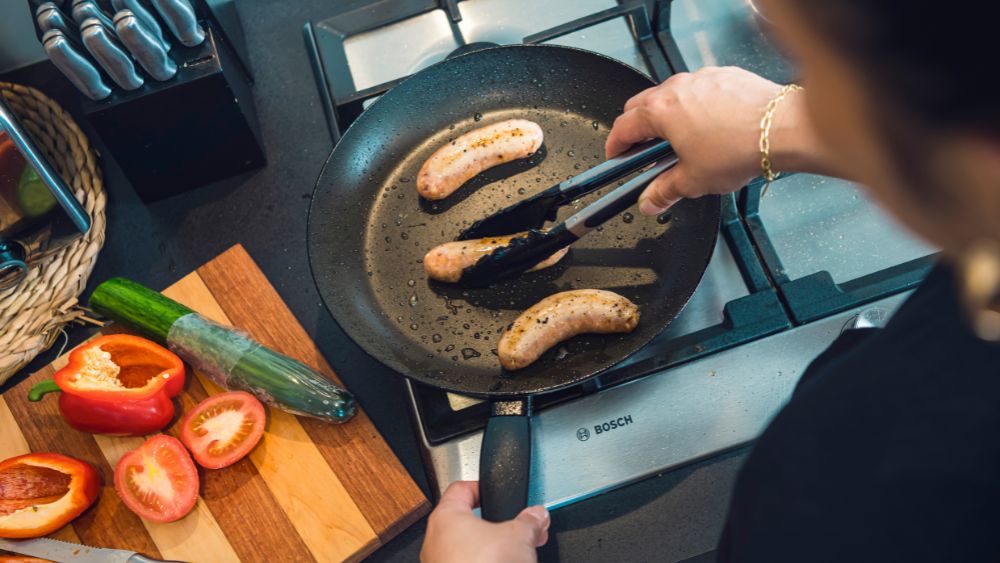 Cooking sausages in a pan on a gas stove top.