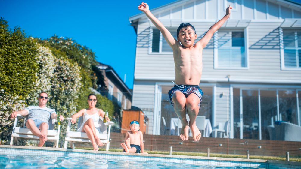Boy jumping into pool as his family watch.