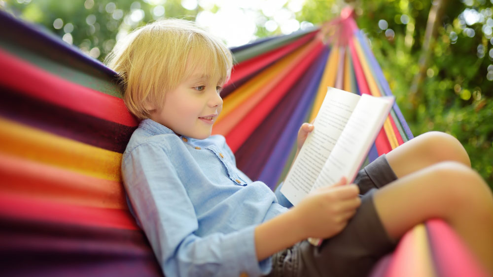 young boy reading in rainbow hammock