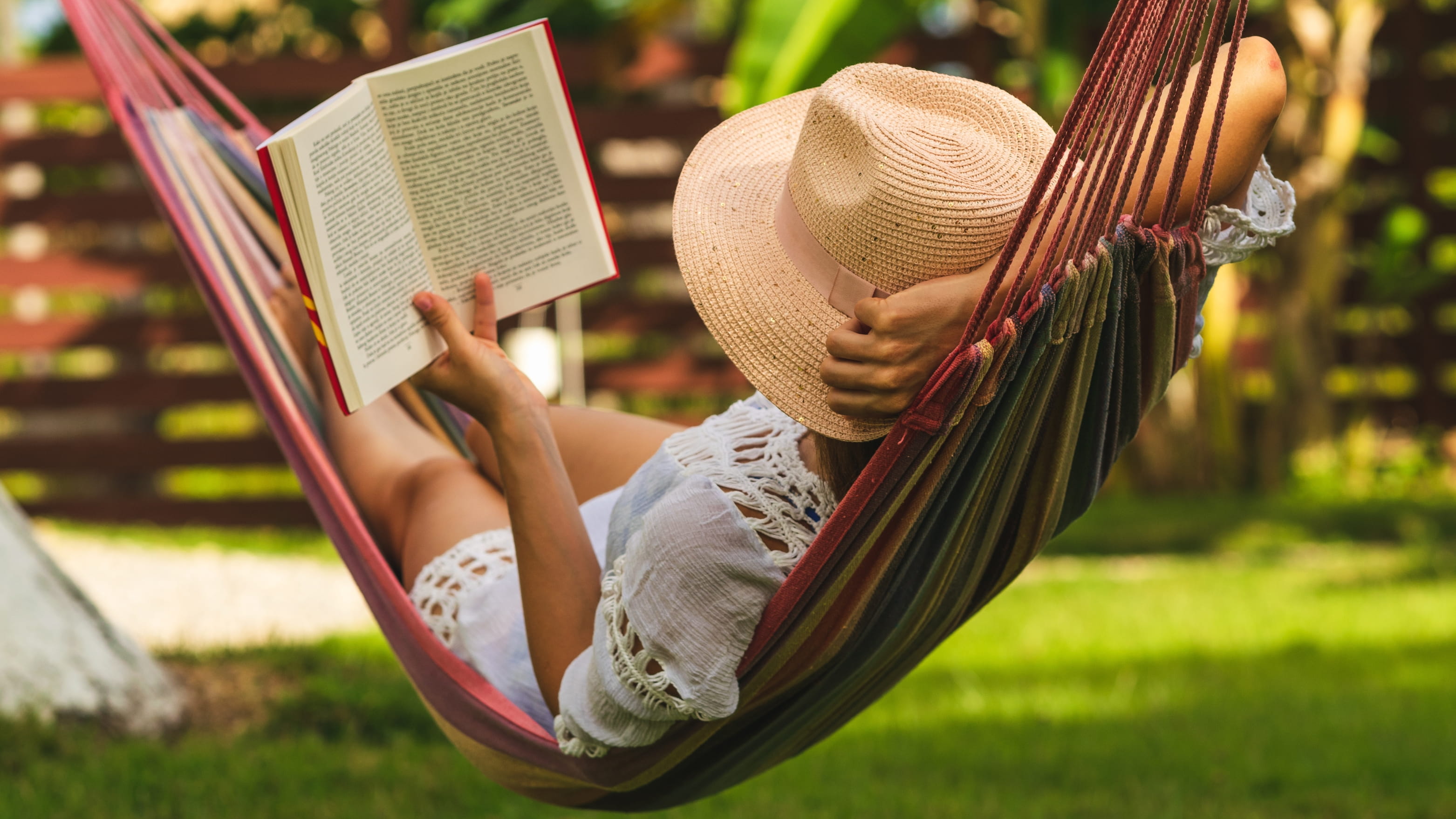 Woman reading in hammock with a hat on.