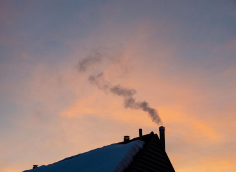 Roof top at sunset with smoke coming out of chimney.