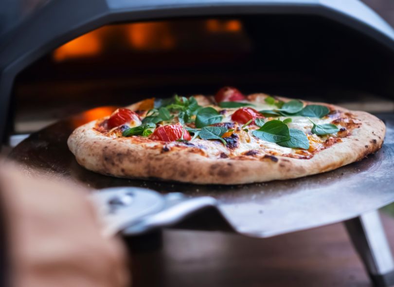 Pizza on a pizza paddle into a gas pizza oven.