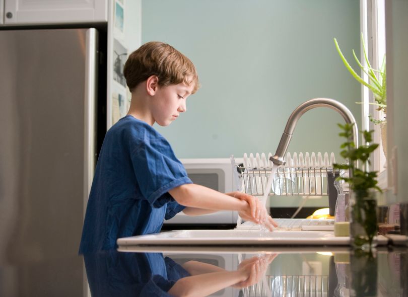 Child washing their hands in the kitchen.