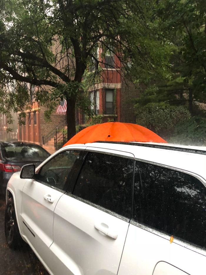 Car with umbrella shielding from the rain.