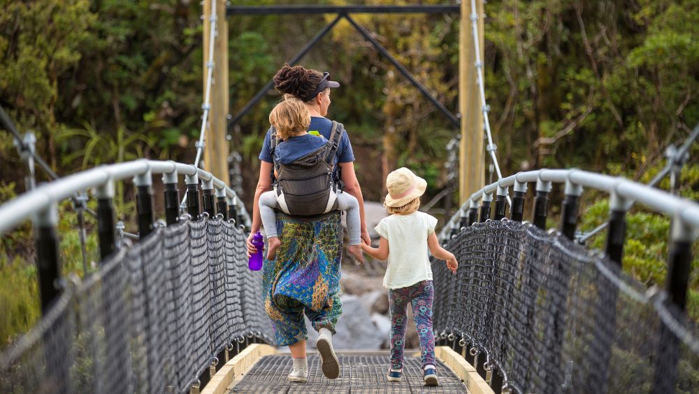 Woman walking over bridge carrying two children.