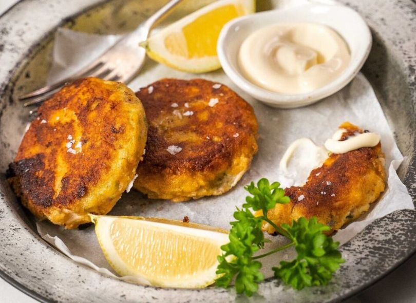 Fish cakes on a plate with slices of lemon and tartare sauce.