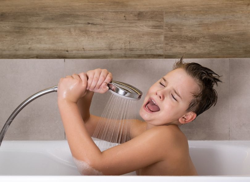 Boy in bath singing into tap.