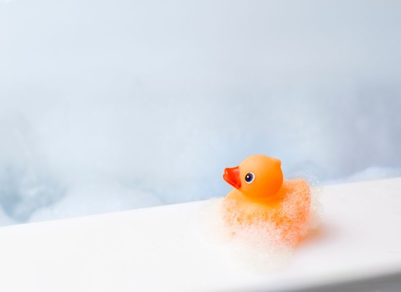 Rubber ducky sitting on the edge of a bubble bath.