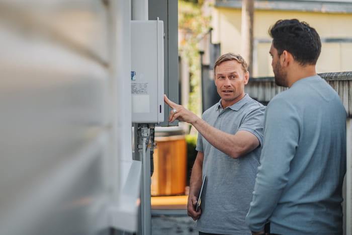 gasfitter and customer looking at gas heating panel on house