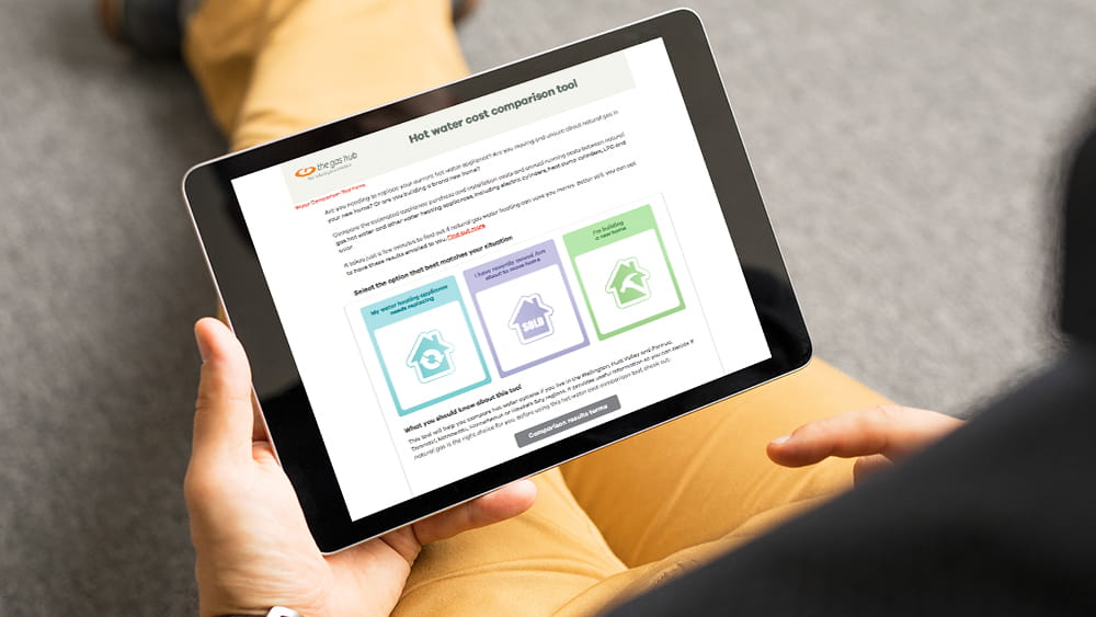 Man sitting with iPad showing The Gas Hub water heating cost comparison tool