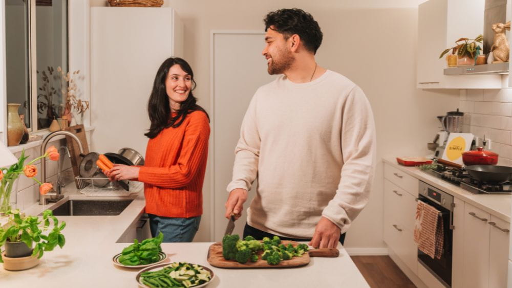 A man and woman preparing vegetables in the kitchen.