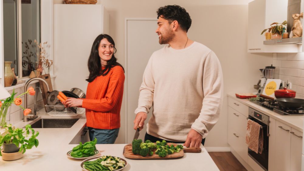 A man and woman preparing vegetables in the kitchen.